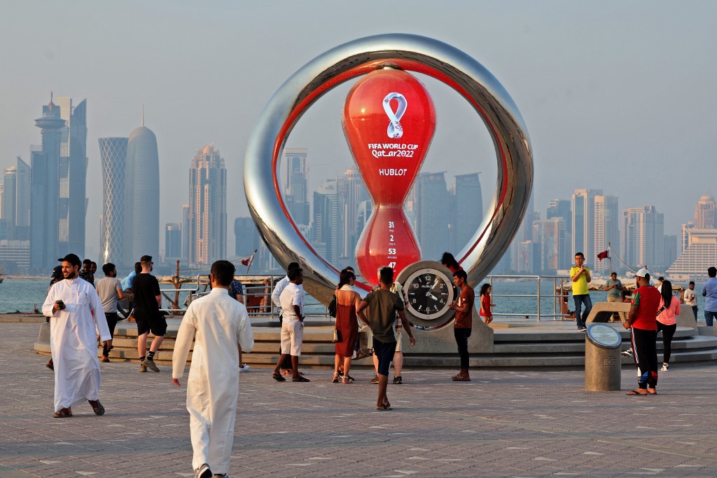 A picture taken on October 20, 2022, shows people walking past the Qatar 2022 FIFA World Cup countdown clock as it nears marking thirty days, in the Qatari capital Doha. (Photo by Karim JAAFAR / AFP)