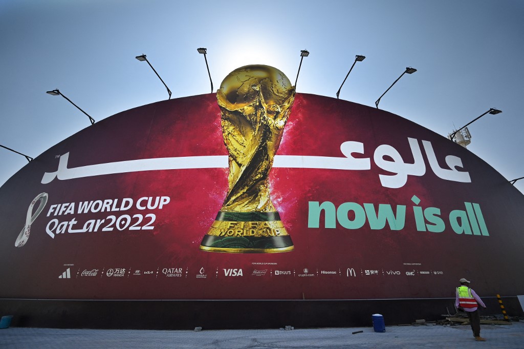 A worker walks in front of a Qatar 2022 FIFA World Cup football tournament billboard in Doha on October 29, 2022. (Photo by Gabriel BOUYS / AFP)